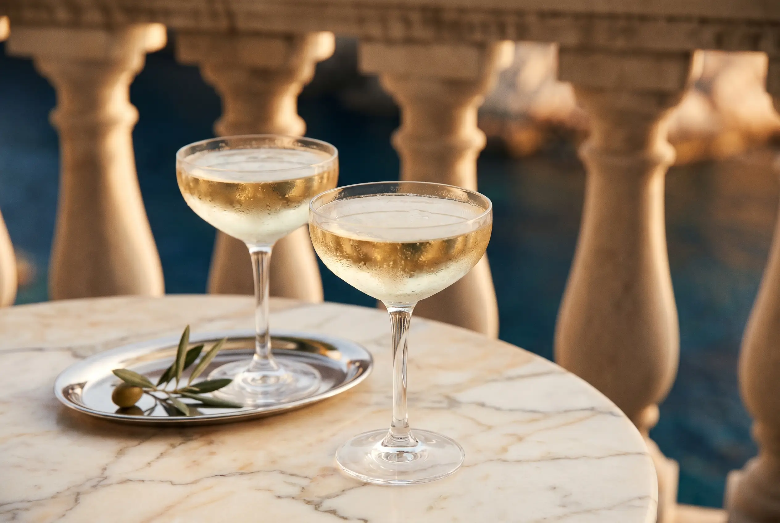 Two coupes of champagne on a marble terrace at golden hour